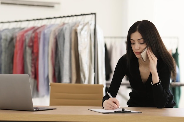 Lady administrator of dry cleaning talks to client on mobile phone making notes on clipboard