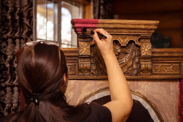 Lady in the beginning of restoring carved ornaments of antique\
cupboard for kitchen with window in background reusage of old\
furniture for sustainable future hobby of furniture\
restoration