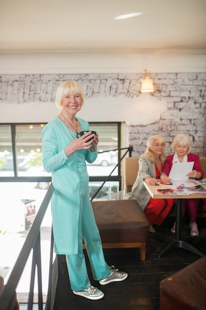 Lady in blue. A blonde woman in a blue suit standing with a cup of tea in hands and smiling