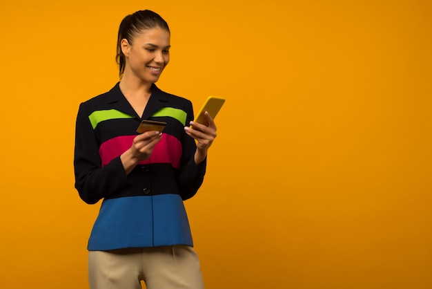 Lady buying online with a credit card and smart phone on yellow background