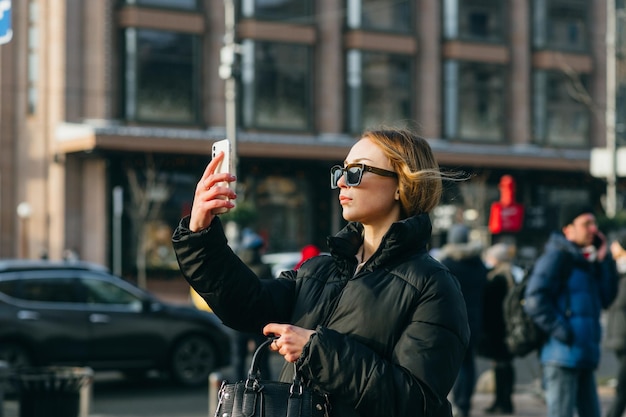 A lady in casual clothes stands on the street of the metropolis and uses a camera on a smartphone