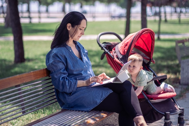 Lady denim shirt writing text on tablet with keyboard and active baby child getting out of stroller