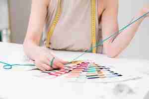 写真 巻尺を持つ女性デザイナーが、洋裁アトリエのテーブルで糸の色と見本を比較する