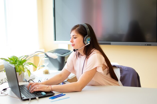 Lady freelancer wearing headset, communicating with client via video computer call.