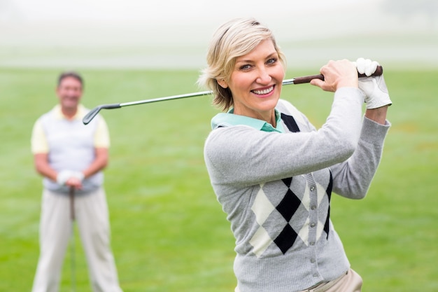 Lady golfer teeing off for the day watched by partner