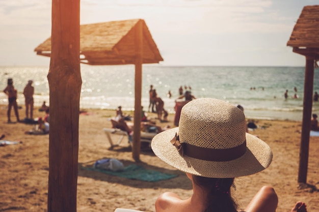 Lady in hat on beach blurred people and sea perfect place for summer rest escape from city bustle