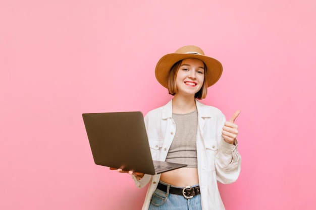 Lady in the hat holds a laptop in hand and rejoices to win and shows thumb up