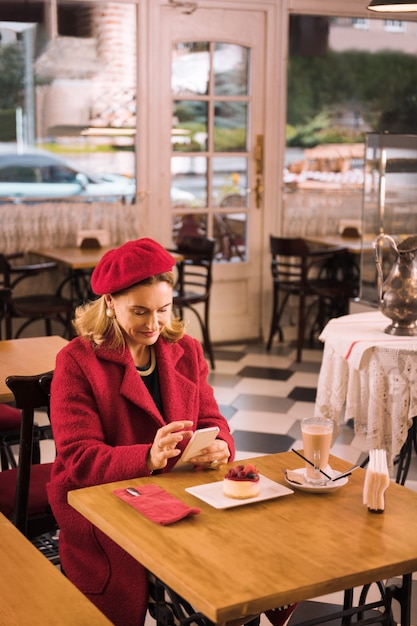Фото Леди в красном. элегантная зрелая дама в красном пальто сидит в кафе, пьет кофе и ест чизкейк