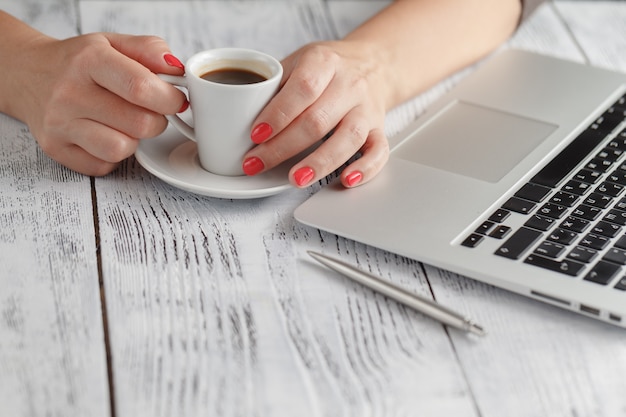 女性がPCの机でコーヒーを手に持っています。