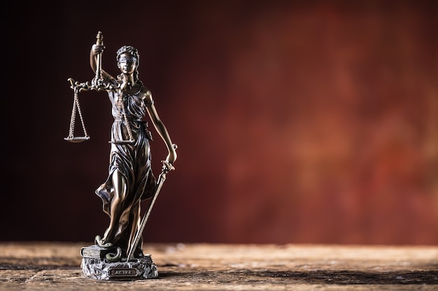 Lady Justicia holding sword and scale bronze figurine on wooden table.