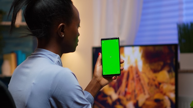 Signora che guarda lo smartphone con schermo verde mentre si rilassa a casa seduta sul divano. donna che tiene un telefono cellulare con il display del telefono cellulare isolato chiave di crominanza modello mockup utilizzando la tecnologia internet