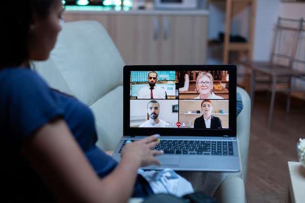 Lady in pajamas sitting on sofa having online meeting with project partners