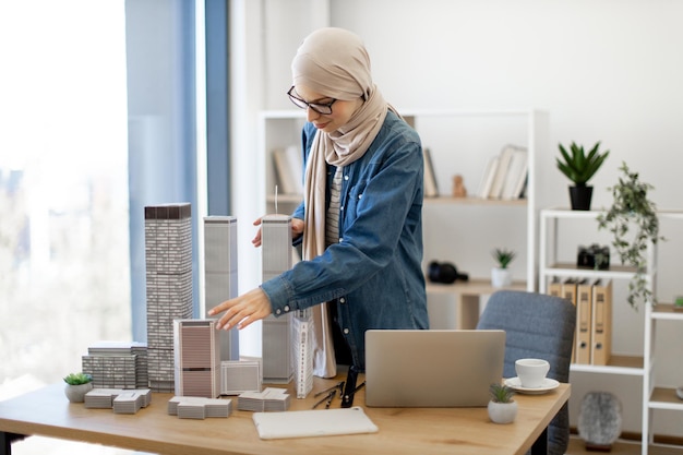 Lady placing scale models on office desk near laptop