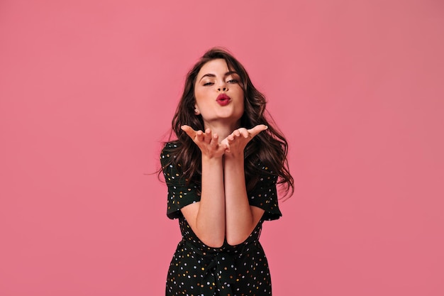 Lady in polka dot dress blows kiss on pink background Lovely girl with painted lips and fashionable makeup blows kiss