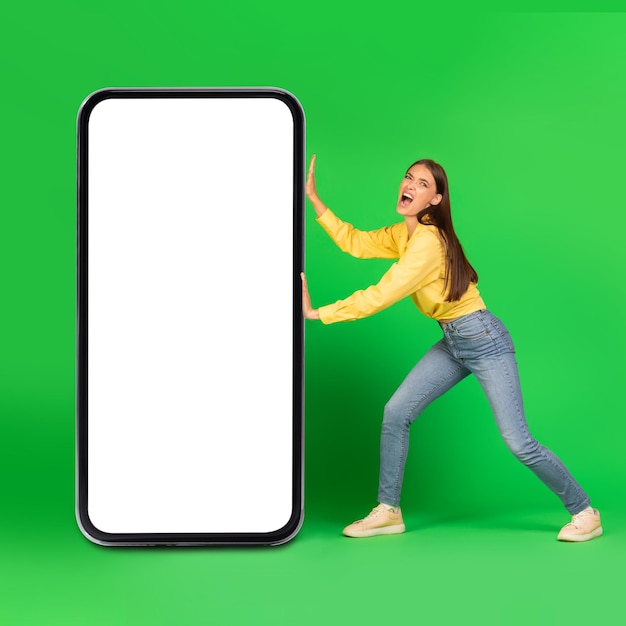 Lady pushing big cellphone blank screen posing over green background