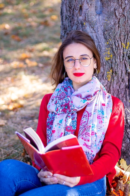 Lady in red sweater reads in nature. Girl and book