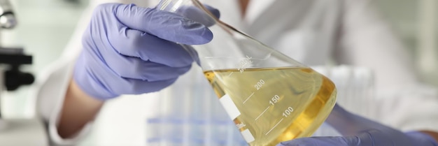 Lady scientist in rubber gloves holds glass flask with oil in hands sitting at table woman