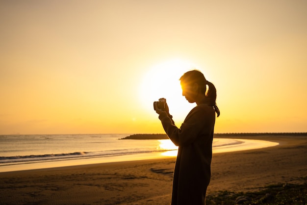 Lady silhouette with using camera to take photo at seaside beach