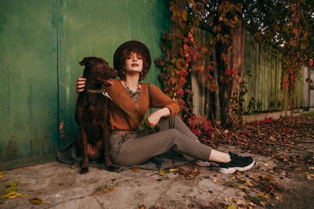 Foto signora seduta sulla strada di una casa di campagna con un bel cane e guardando nella telecamera