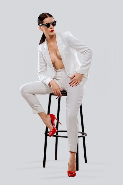 Lady in white pantsuit and sunglasses sitting on chair