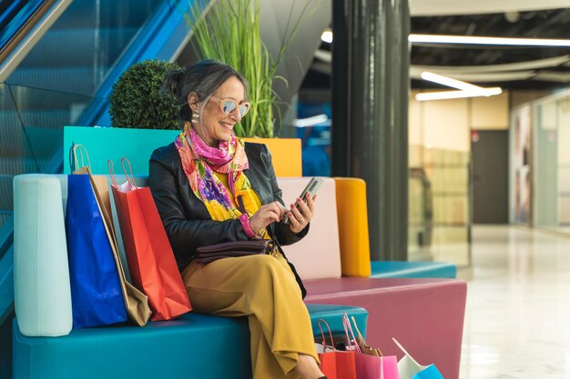 Lady with shopping bags sitting and chatting on mobile phone in a mall happy smiling senior woman