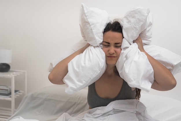Фото Женщина с нарушениями сна прижимает подушки к голове страдает от приступов мигрени и бессонницы