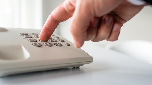 Lage hoek close-up weergave van mannenhand die een telefoonnummer kiest op een witte vaste telefoon