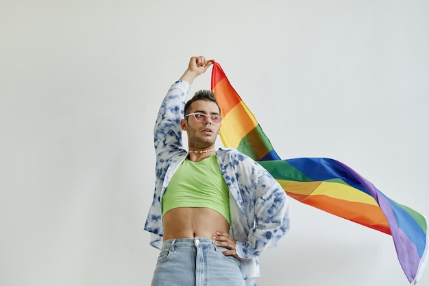 Lage hoek portret van zelfverzekerde homoseksuele man trots vlag zwaaien tegen witte achtergrond kopie ruimte
