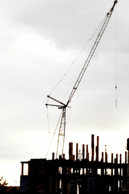 Lage hoek van de silhouetkraan door het gebouw tegen de hemel tijdens de zonsondergang
