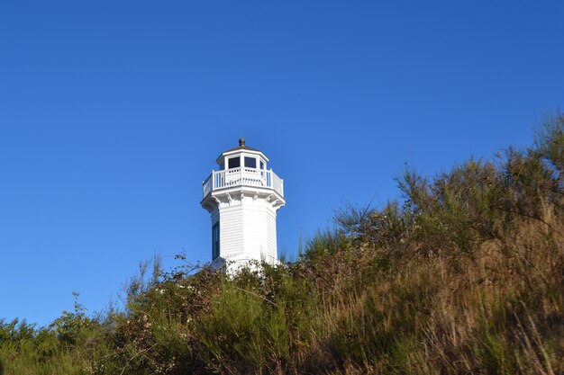 Foto lage hoek van de vuurtoren op de heuvel tegen een heldere blauwe lucht