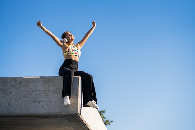 Lage hoek van een jonge vrouw die op een muur zit tegen de blauwe lucht