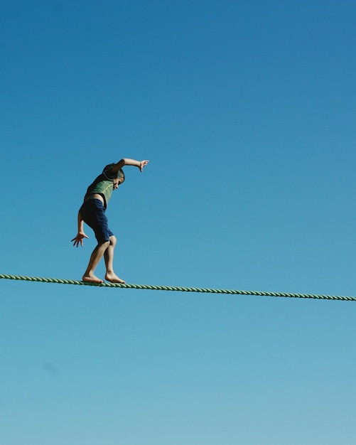 Foto lage hoek van een jongen die op een touw loopt tegen een heldere blauwe lucht tijdens een zonnige dag