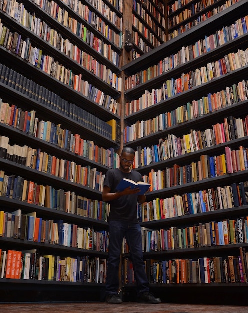 Lage hoek van een man die een boek leest terwijl hij bij boekenplanken in de bibliotheek staat