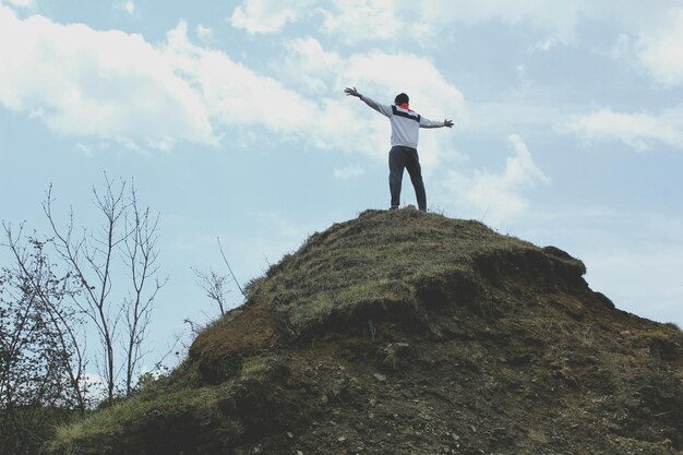 Foto lage hoek van een man met uitgestrekte armen die op een klif tegen de lucht staat