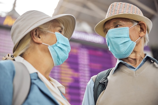 Lage hoek van een ouder Kaukasisch stel met beschermende wegwerpmaskers die elkaar aanstaren