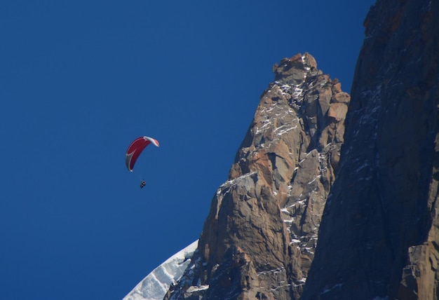 Foto lage hoek van een persoon die met een paraglider tegen een heldere blauwe lucht vliegt