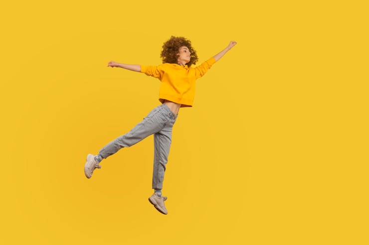 Foto lage hoek van een persoon die tegen een gele achtergrond springt