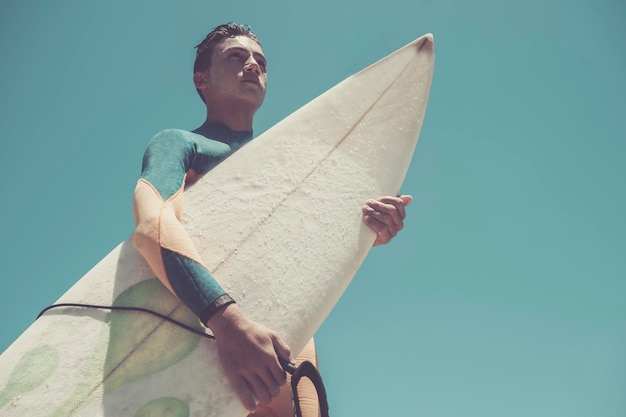 Lage hoek van een tiener die een surfplank vasthoudt tegen een heldere blauwe lucht