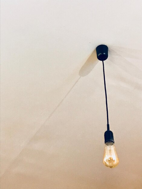 Foto lage hoek van een verlichte gloeilamp die aan de muur hangt