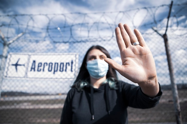 Foto lage hoek van een vrouw die een masker draagt en een stopteken tegen een hek toont