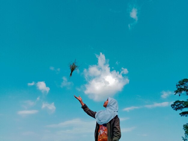 Foto lage hoek van een vrouw die een plant tegen de lucht gooit