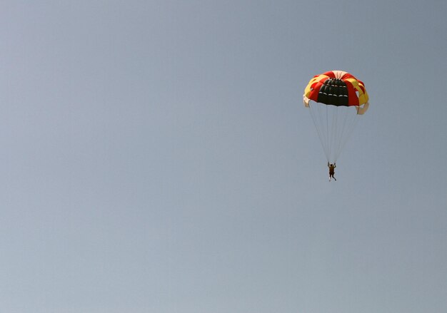 Lage hoek van een vrouw die met een paraglider tegen een heldere lucht vliegt