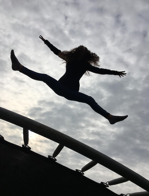 Lage hoek van een vrouw die over een trampoline springt tegen een bewolkte lucht