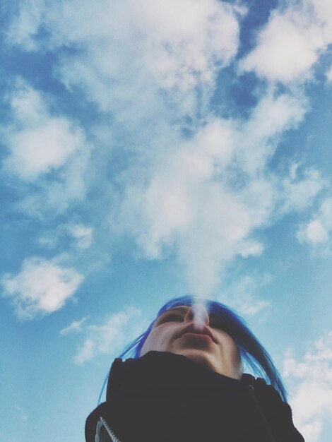 Foto lage hoek van een vrouw die tegen de lucht rookt