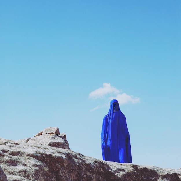 Lage hoek van een vrouw in boerka die op een rotsformatie staat tegen de blauwe hemel tijdens een zonnige dag