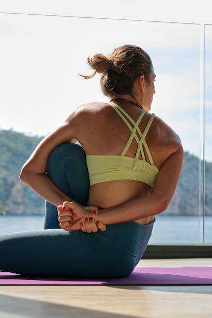 Lage hoek van flexibele vrouw in sportkleding die yoga doet in Sage Marichi pose terwijl ze in de zomer op de mat op het terras zit