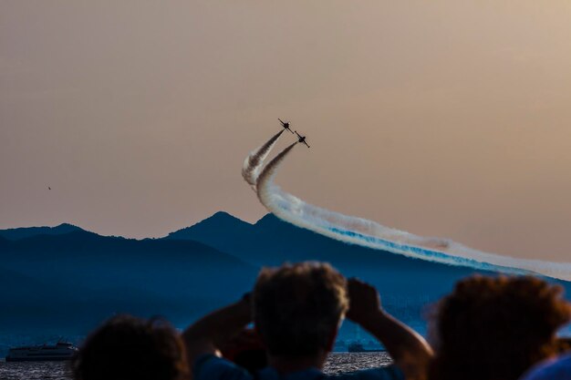 Foto lage hoek van mensen die naar een luchtshow kijken tegen de lucht