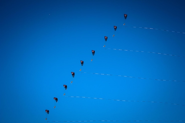 Foto lage hoek van mensen die paragliden tegen een heldere blauwe hemel tijdens een zonnige dag