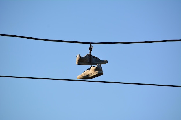 Lage hoek van schoenen die aan een kabel hangen tegen een heldere blauwe lucht