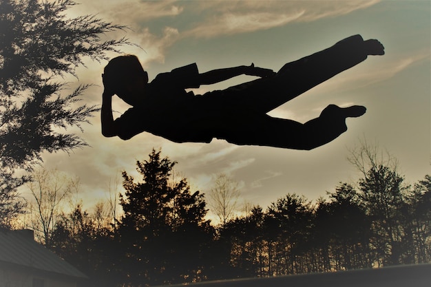 Foto lage hoek van silhouet man die tegen bomen springt